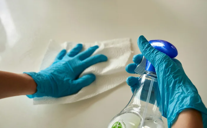 Gloved hands disinfecting a frequently touched surface
